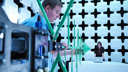 Engineers checking a bilog antenna for electromagnetic compatibility (EMC) radiated immunity testing in a semi anechoic chamber relative to the electronic equipment under test