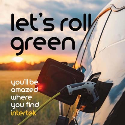 Electric vehicle with charge cable inserted while in a grassy field with the sun near the horizon